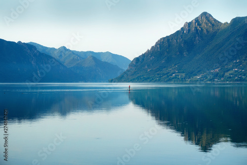 Fisherman in traditional conoe swimming on lake at the morning scenery with light fog and mountain landscape.