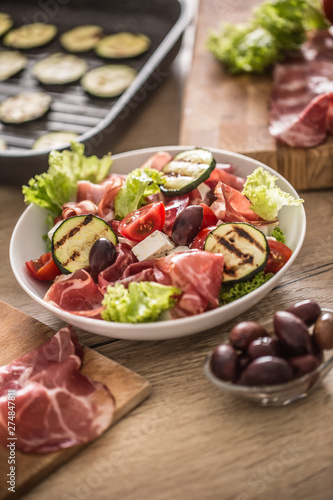 Fresh lettuce salad with grilled zucchini coppa di parma ham feta cheese olives tomatoes and olive oil