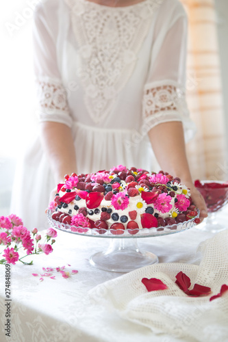 White isolated background with clipping paths homemade Berry Fruit cake, homemade biscuit cake with cream, in woman hands against of light summer flowers background