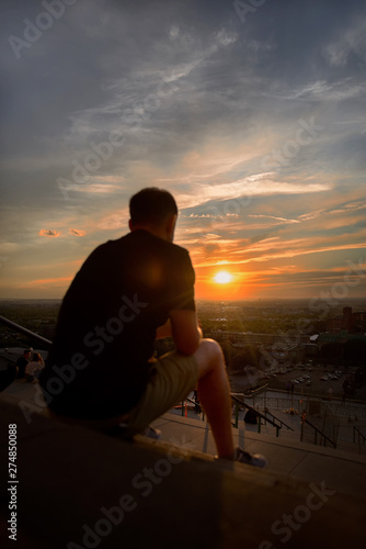 Man  a man sitting on a stair watching the sunset over Montreal on a summer evening. Travel to Canada