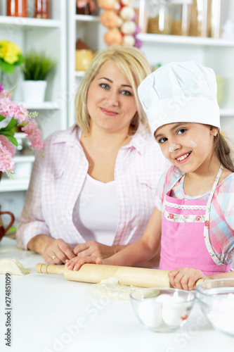 Cute girl in white hat with her mother making dough