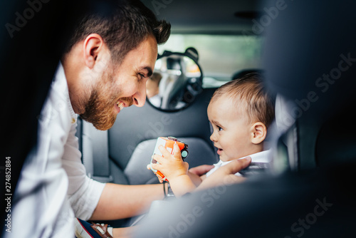 Smiling father putting baby in child seat, fastening seatbelt - Family transportation, lifestyle concept photo