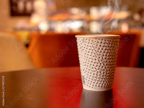 Paper cup with hot coffee or tea on a table in a cafe