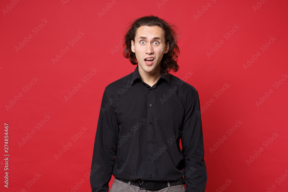 Young sad curly long haired man in black shirt standing posing isolated on red wall background studio portrait. People sincere emotions lifestyle concept. Mock up copy space. Problem crisis depression Young sad curly long haired man in black shirt standing posing isolated on red wall background studio portrait. People sincere emotions lifestyle concept. Mock up copy space. Problem crisis depression