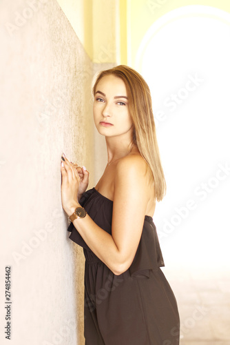 Portrait of young woman in black clothes standing by the wall and looking at camera.