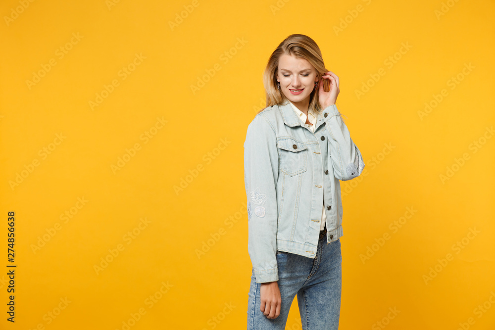 Fototapeta premium Portrait of tender attractive pretty young woman in denim casual clothes touching hair, keeping eyes closed isolated on bright yellow orange background. People lifestyle concept. Mock up copy space.