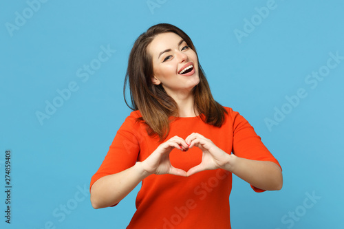 Beautiful brunette young woman wearing red orange dresss howing shape heart sign with hands, isolated over blue wall background, studio portrait. People lifestyle fashion concept. Mock up copy space. photo