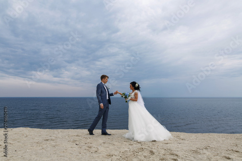 stylish brides walking on the sandy beach. groom hugging bride and walking on beach.wedding day. wedding walks.stylish couple in love  © mihail_pustovit