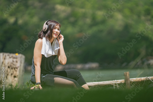 Young happy smiling asian woman listening music with headphones from her smart phone at the park.