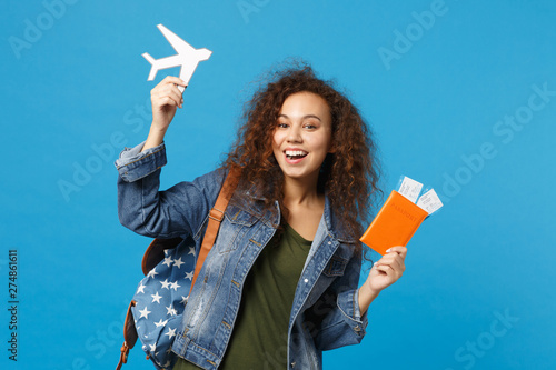 Young african american girl teen student in denim clothes, backpack hold pass isolated on blue wall background studio portrait. Education in high school university college concept. Mock up copy space.