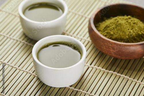 selective focus of white cups with tea near green matcha powder in wooden bowl