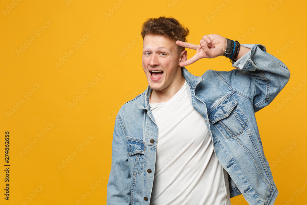 Obraz premium Portrait of cheerful young man in denim casual clothes keeping mouth open showing victory sign isolated on yellow orange wall background. People sincere emotions lifestyle concept. Mock up copy space.