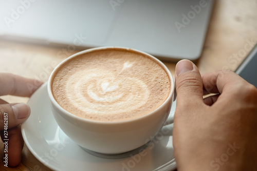 A cup of coffee on desk, Cup of coffee in hand, Men hand hold mug of latte coffee, Close up concept.
