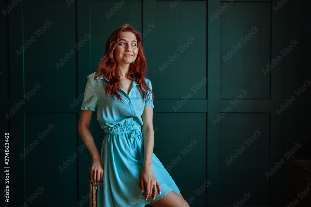 Portrait of a beautiful redhaired girl in a light blue dress on a dark background