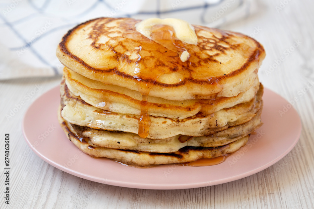 Homemade pancakes with butter and maple syrup on a pink plate, side view. Close-up.