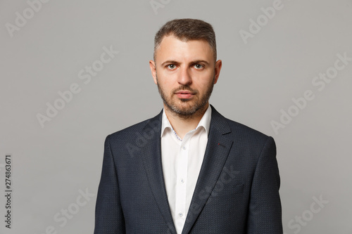 Handsome successful confident young business man in classic black suit shirt posing isolated on grey wall background, studio portrait. Achievement career wealth business concept. Mock up copy space.