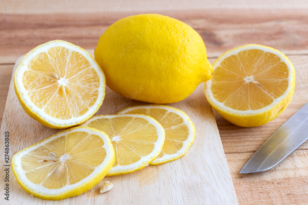 Fresh yellow lemon and slice of lemon with knife on a wooden table in the kitchen.