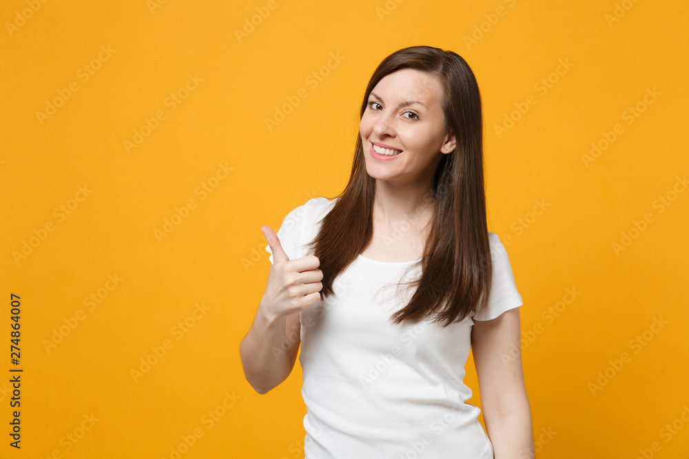 Portrait of smiling beautiful young woman in white casual clothes looking camera, showing thumb up isolated on bright yellow orange background in studio. People lifestyle concept. Mock up copy space. Portrait of smiling beautiful young woman in white casual clothes looking camera, showing thumb up isolated on bright yellow orange background in studio. People lifestyle concept. Mock up copy space.