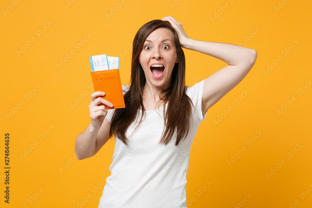 Excited young woman in white clothes keeping mouth open, putting hand on head, holdpass port, boarding pass tickets isolated on yellow orange background. People lifestyle concept. Mock up copy space. Excited young woman in white clothes keeping mouth open, putting hand on head, holdpass port, boarding pass tickets isolated on yellow orange background. People lifestyle concept. Mock up copy space.