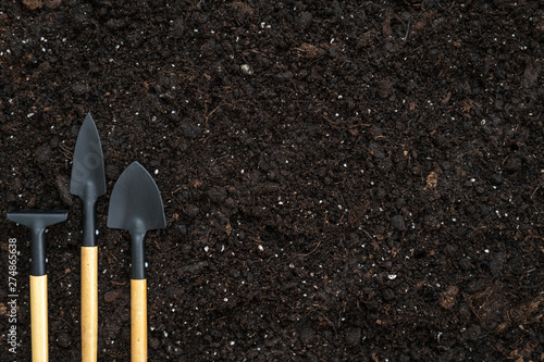 Set gardening tools, rake and shovels on black soil ground with copy space
