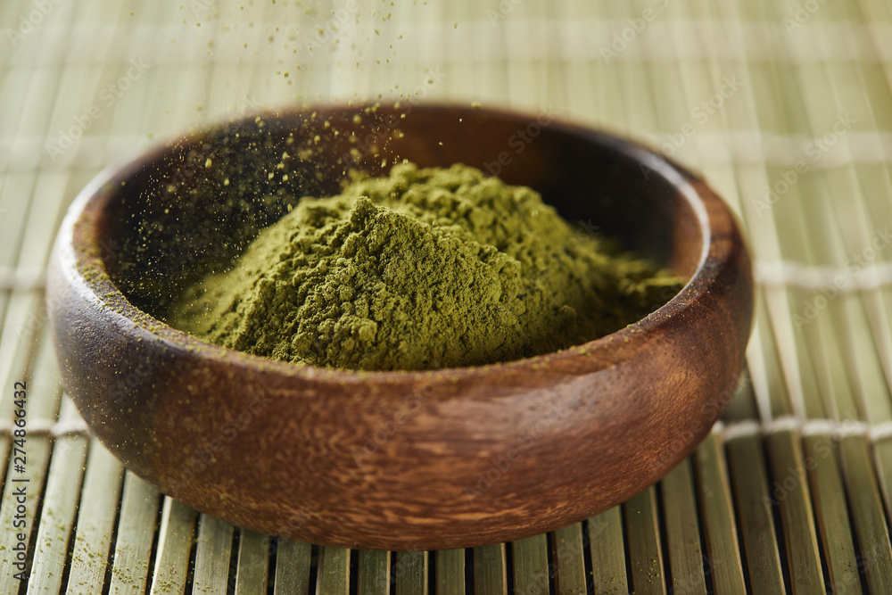 selective focus of green matcha powder pouring in wooden bowl on bamboo table mat selective focus of green matcha powder pouring in wooden bowl on bamboo table mat