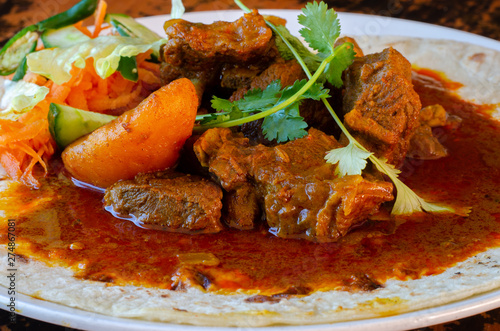 A mutton curry roti with sambals - an iconic Durban meal consisting of a roti topped with mutton curry and gravy. The sambals are grated carrot with chopped chilli.