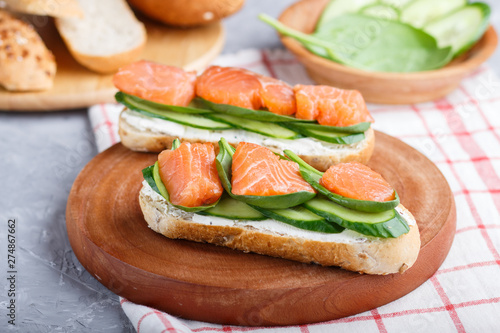 Smoked salmon sandwiches with cucumber and spinach on wooden board on a linen background.