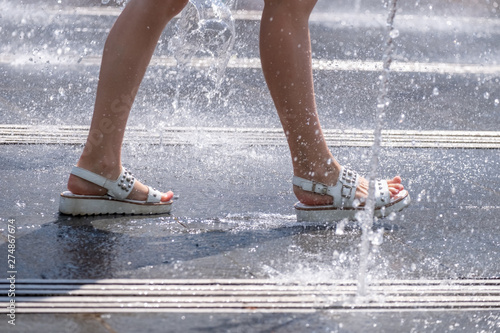 Women's feet in sandals in the midst of a refreshing spray of the city fountain on a hot summer day