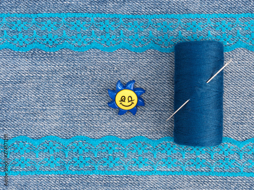 Tailor's tools – blue lace, threads with needle, button on a jeans backgroud. Stitching still life photo