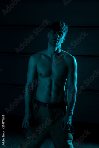 sexy shirtless fireman in pants looking at camera in darkness