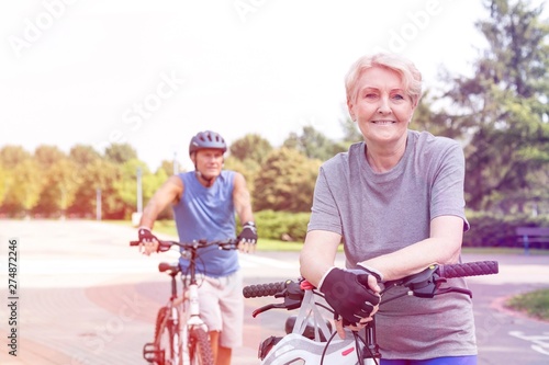 Confident senior woman leaning on bicycle in park