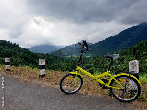 A yellow bike on the road to Khun Dan Prakan Chon Dam, Naknon Nayok, Thailand, ithe the light beam through clouds in the background