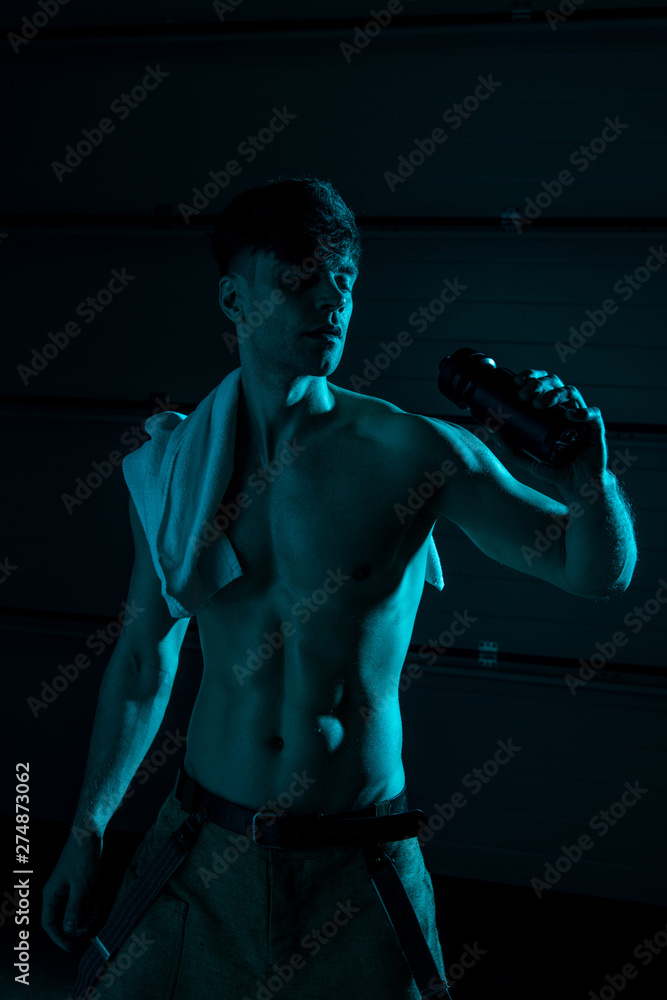 sexy shirtless man with towel holding sport bottle in darkness