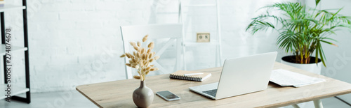 panoramic shot of laptop and smartphone on wooden table in modern office