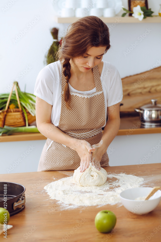 Young brunette woman cooking pizza or handmade pasta in the kitchen. Housewife preparing dough on wooden table. Dieting, food and health concept Young brunette woman cooking pizza or handmade pasta in the kitchen. Housewife preparing dough on wooden table. Dieting, food and health concept