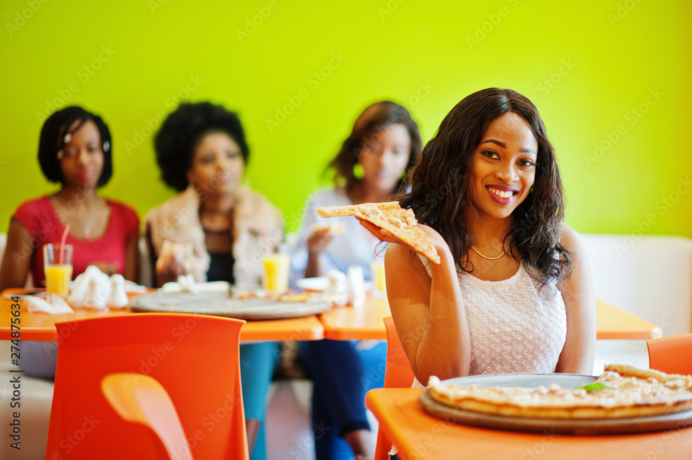 African woman with pizza sitting at restaurant against dark skinned girls.