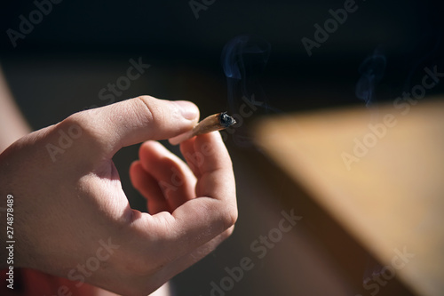 The man holds in his hand with his fingers the butt of a Smoking  smoke cigarette  which is illuminated by bright warm sunlight.