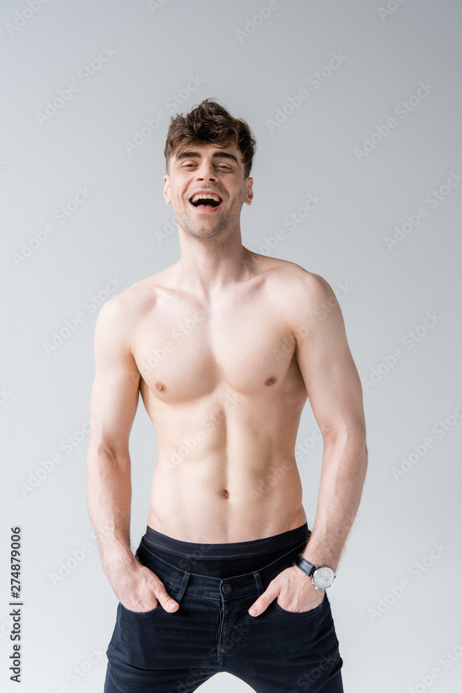 laughing shirtless man with hands in pockets isolated on grey laughing shirtless man with hands in pockets isolated on grey