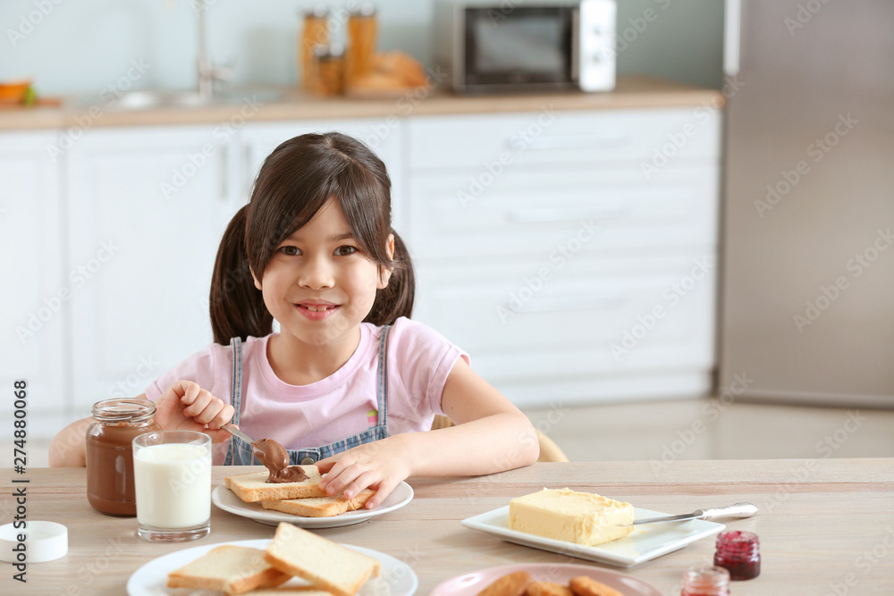 Funny little girl eating tasty toasts with chocolate spreading in kitchen Funny little girl eating tasty toasts with chocolate spreading in kitchen