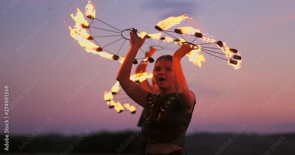 Fire dancers against sunset. A young woman poses with her fire hoop against the sunset during her dance performance.