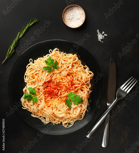 italian pasta spaghetti with tomato sauce, on a plate against the background of dark stone. View from above,
