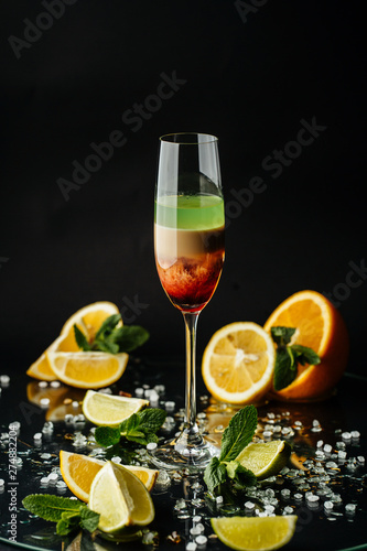 Colorful cocktail in glass with orange and lemon on dark background.