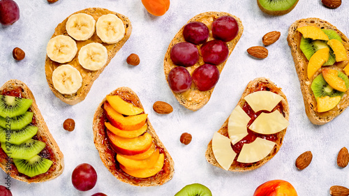 Fototapeta Naklejka Na Ścianę i Meble -  Healthy breakfast toasts with peanut butter, strawberry jam, banana, grapes, peach, kiwi, pineapple, nuts. Copy space