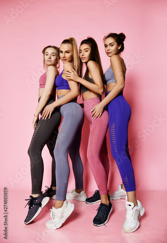 Young tall athletic women in blue, grey, brown standing behind each other. Fitness girls posing on pink background. 