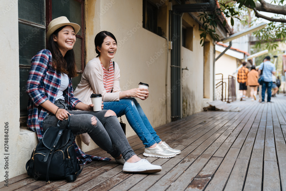 two happy young girls friends relax sitting outdoor leaning on old house window in little village. female japanese travelers visit in taiwan taipei small town with beautiful sunset light real moment two happy young girls friends relax sitting outdoor leaning on old house window in little village. female japanese travelers visit in taiwan taipei small town with beautiful sunset light real moment
