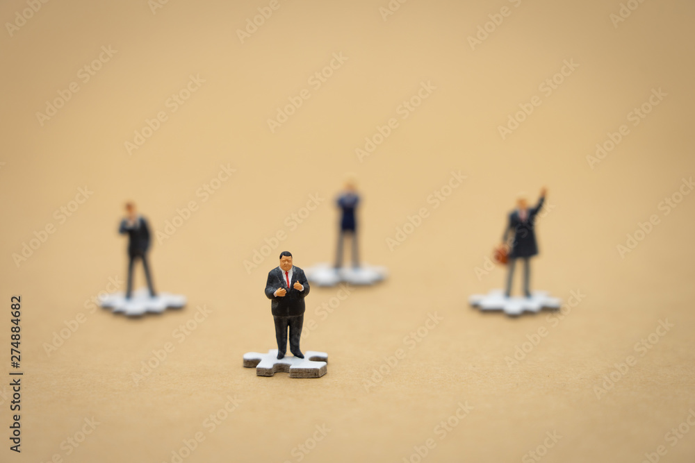 Miniature people businessmen standing on white Jigsaw. The concept used in selecting personnel to participate in the organization. with copy space. Miniature people businessmen standing on white Jigsaw. The concept used in selecting personnel to participate in the organization. with copy space.