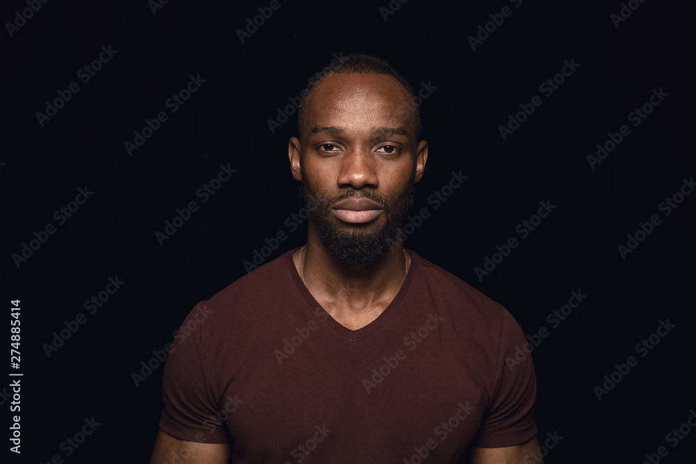 Close up portrait of young african man isolated on black studio background. Photoshot of real emotions of male model. Standing and looks serious. Facial expression, human nature and emotions concept. Close up portrait of young african man isolated on black studio background. Photoshot of real emotions of male model. Standing and looks serious. Facial expression, human nature and emotions concept.