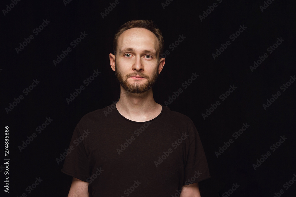 Fototapeta premium Close up portrait of young caucasian man isolated on black studio background. Photoshot of real emotions of male model. Standing and looks serious. Facial expression, human nature and emotions concept
