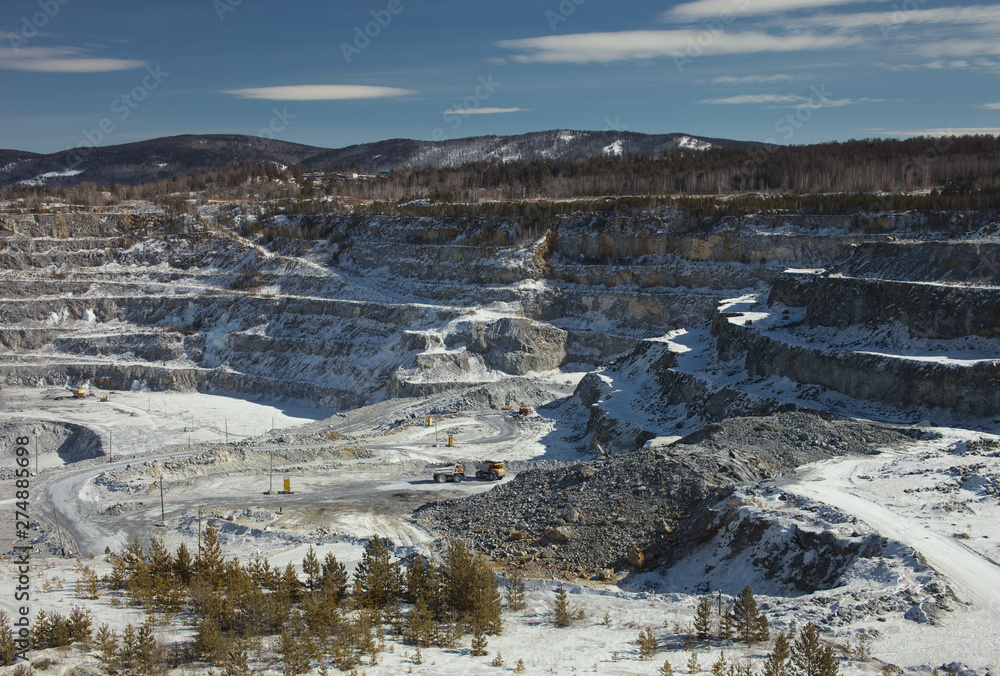 View from the side to the quarry for limestone mining on a winter sunny day. Mining industry. Quarry mining equipment.