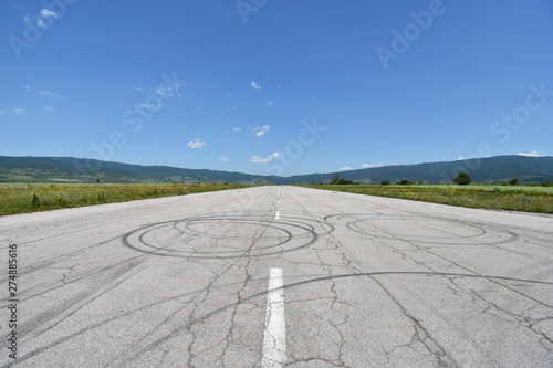 Deserted military airport runway near Sapareva Banya, Bulgaria, nowadays used for amateur car races, cracks and tire tracks seen on the old asphalt surface